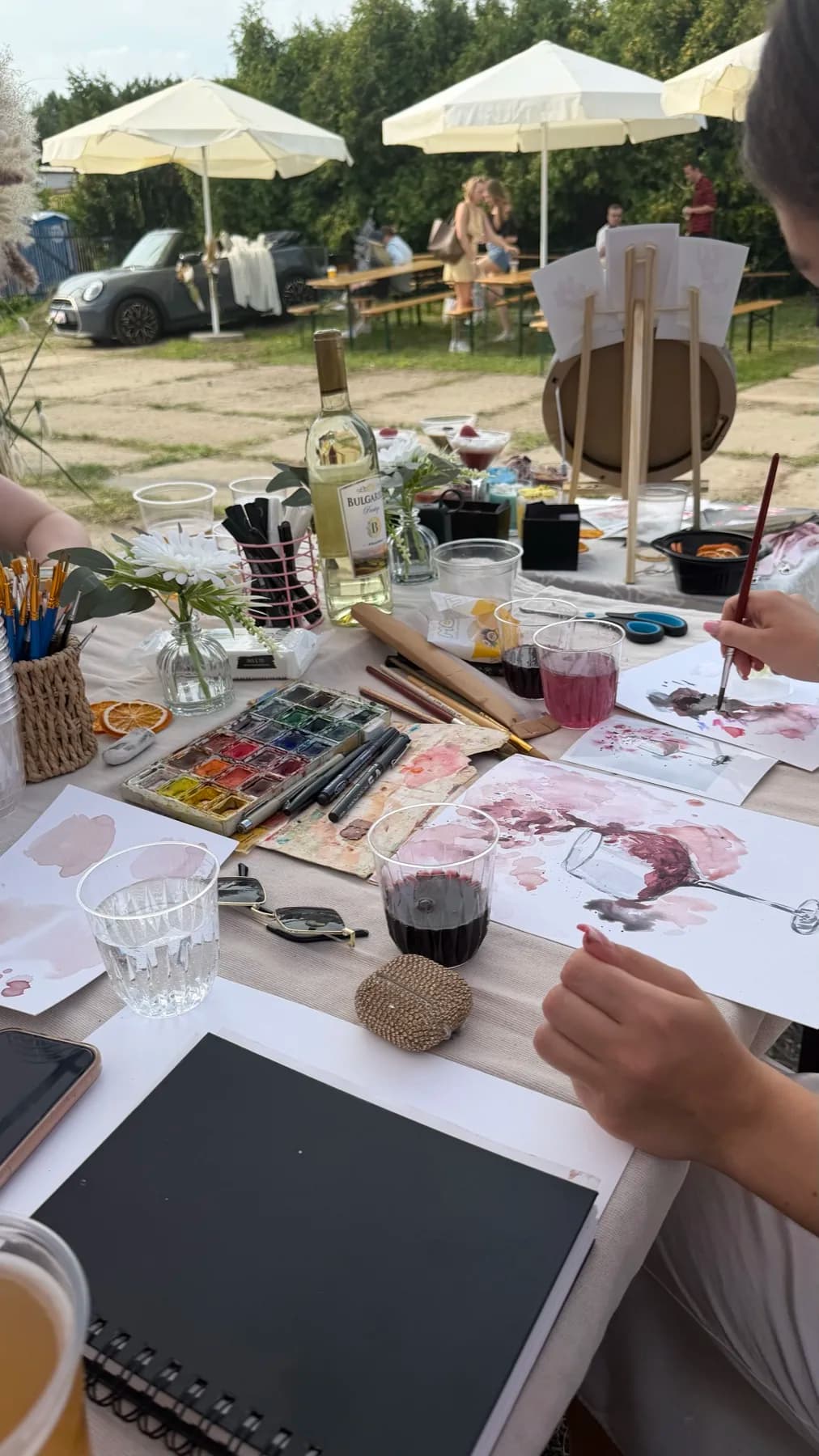 Wine-painting workshop table with wine, brushes, and guest artwork
